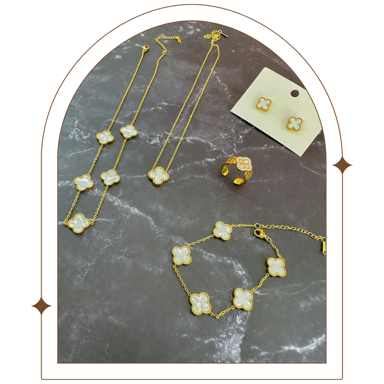 Gold-plated jewelry set on a dark marble surface, featuring a bracelet, necklace, earrings, and a clover-shaped ring with pearl and rhinestone details. Elegant and timeless, perfect for adding sophistication to any look