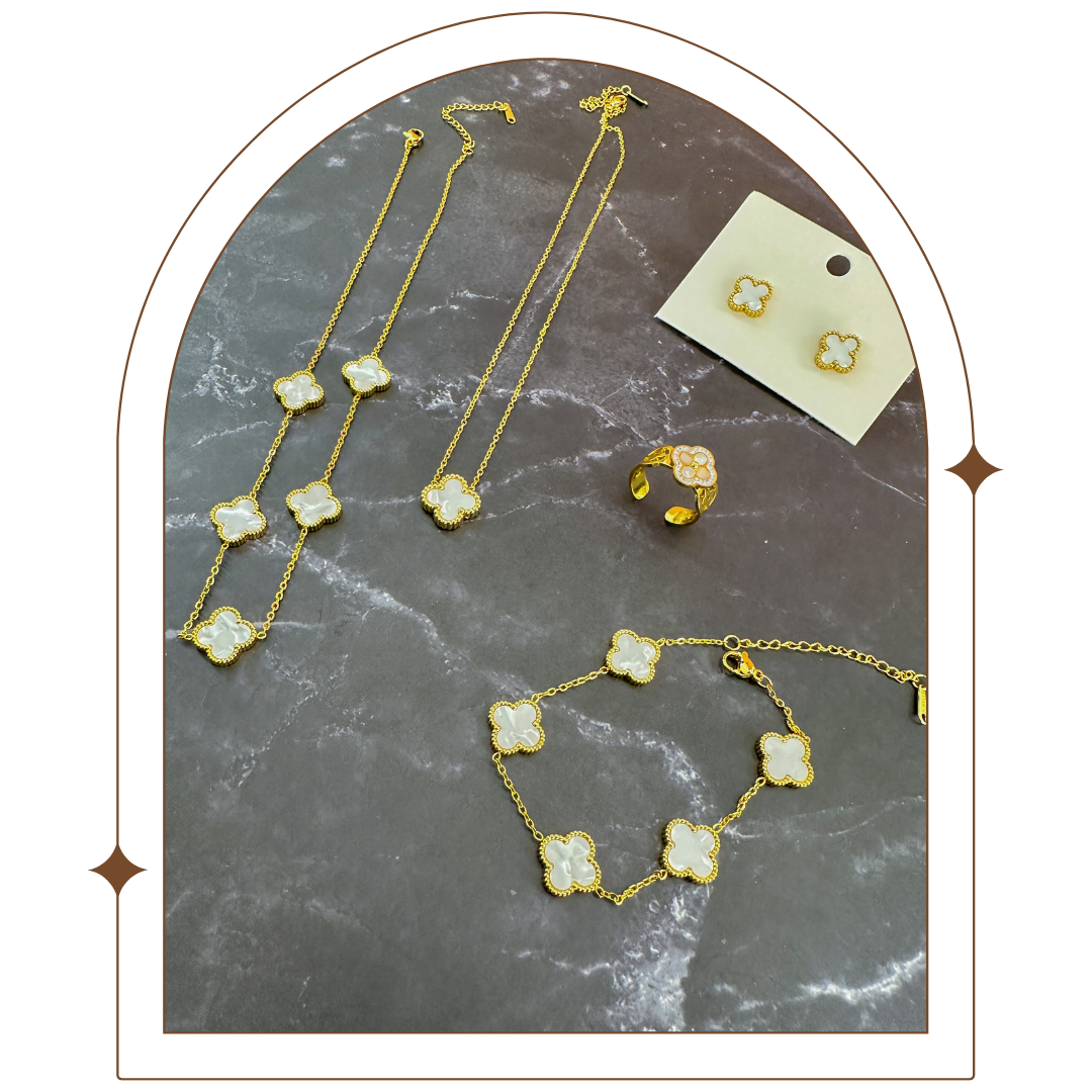 Gold-plated jewelry set on a dark marble surface, featuring a bracelet, necklace, earrings, and a clover-shaped ring with pearl and rhinestone details. Elegant and timeless, perfect for adding sophistication to any look