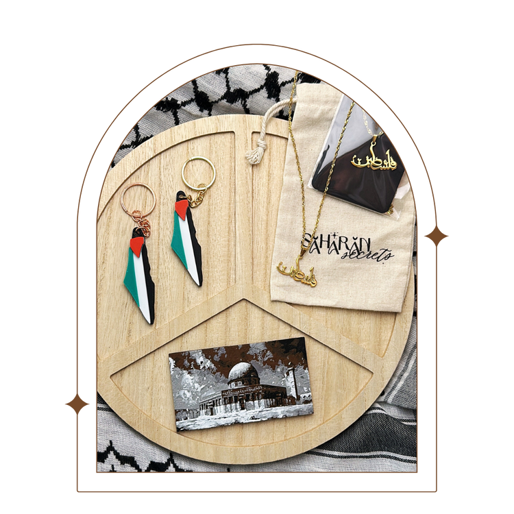 Collection of Palestinian solidarity items including a pair of Palestine flag keychains, a Falasteen necklace, and an Al Aqsa Dome of the Rock magnet displayed on a wooden peace sign background. Perfect for showing support and unity with Palestine.