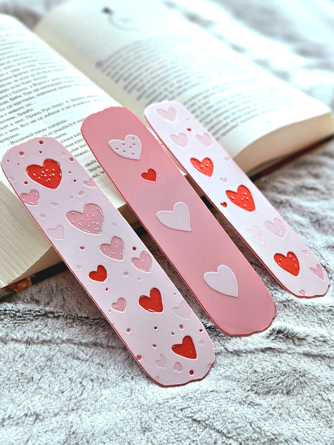 Pink bookmarks with red, pink and white heart patterns laying on a n open book